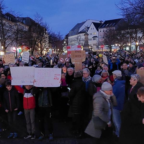 Eine Demonstration auf einem Marktplatz. Menschen halten Protestschilder in die Höhe.
