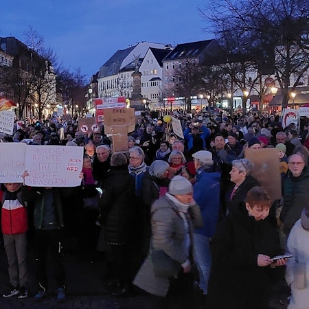 Eine Demonstration auf einem Marktplatz. Menschen halten Protestschilder in die Höhe.