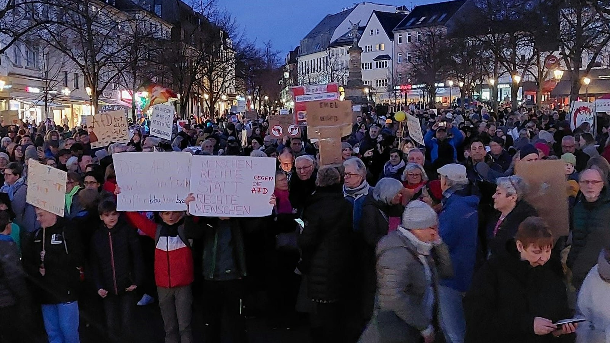 Eine Demonstration auf einem Marktplatz. Menschen halten Protestschilder in die Höhe.
