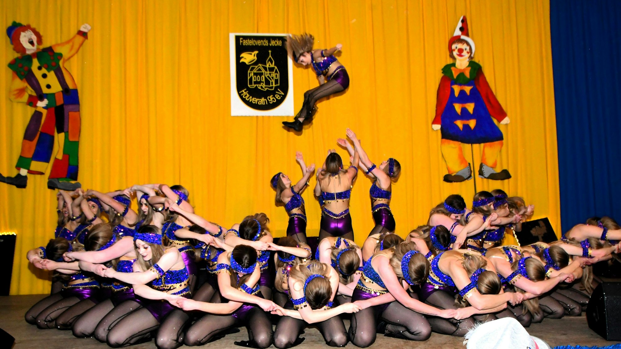 Tänzerinnen knien auf der Bühne, während im Hintergrund ein Mädchen von drei anderen in die Höhe geworfen wird.