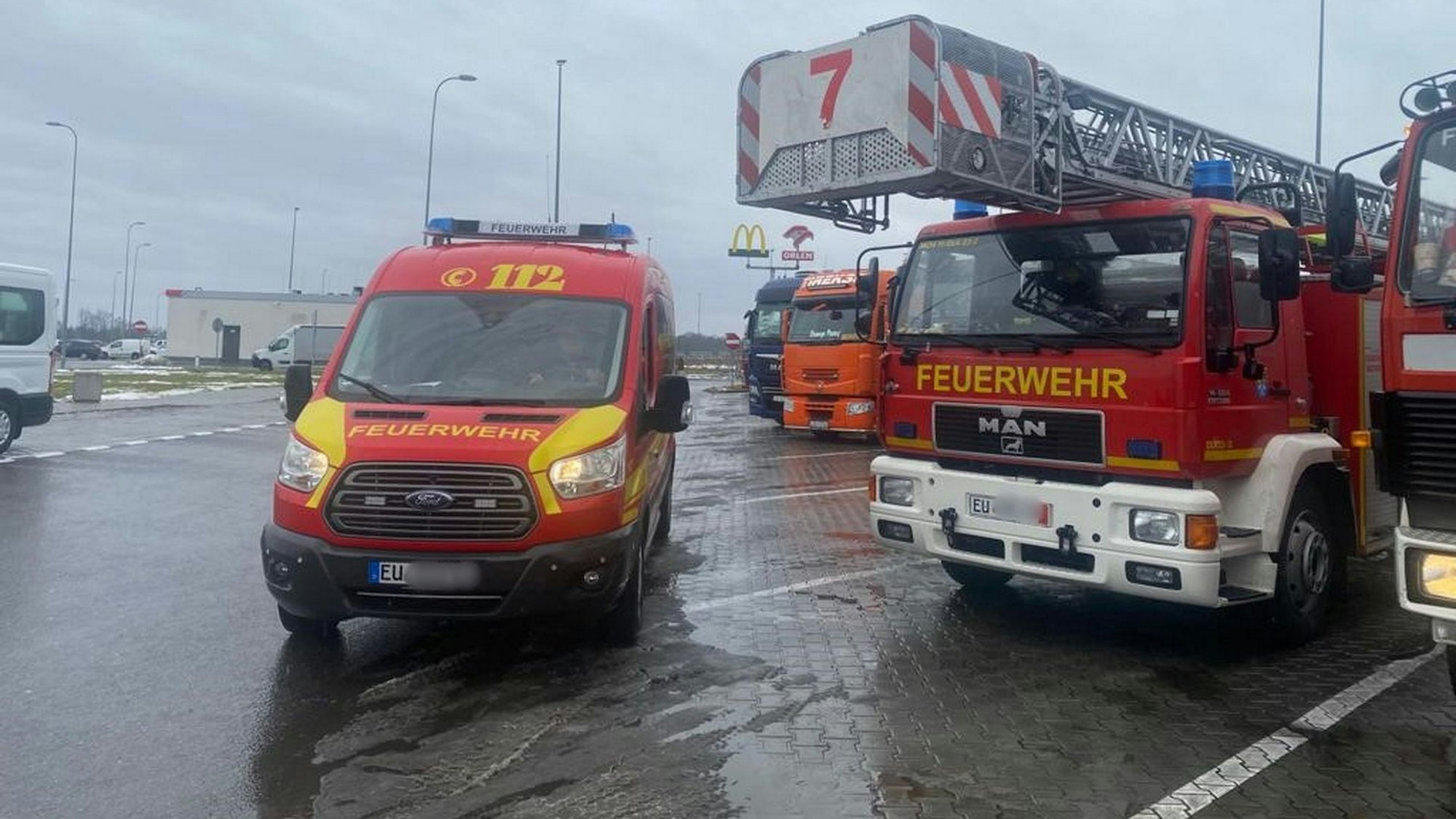 Auf einem Autobahnrastplatz stehen ein Mannschaftstransporter und ein Drehleiterfahrzeug zwischen anderen Lastwagen.