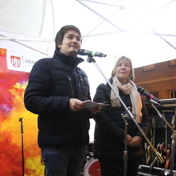 Ein Mann spricht in ein Mikrofon. Neben ihm steht eine Frau.