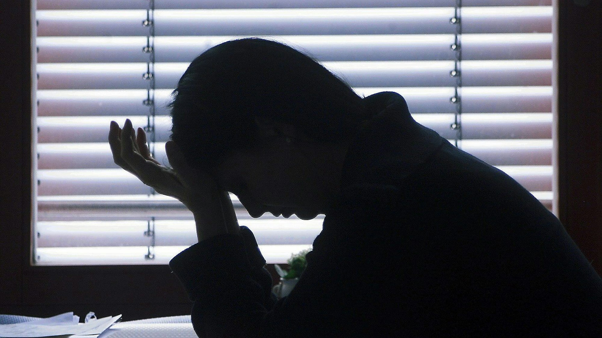 Die Arbeit an einer Förderschule ist für viele Lehrer in NRW extrem belastend. Eine Silhouette ist vor einem Rollo zu sehen: Eine Frau stützt erschöpft ihren Kopf in die Hand.