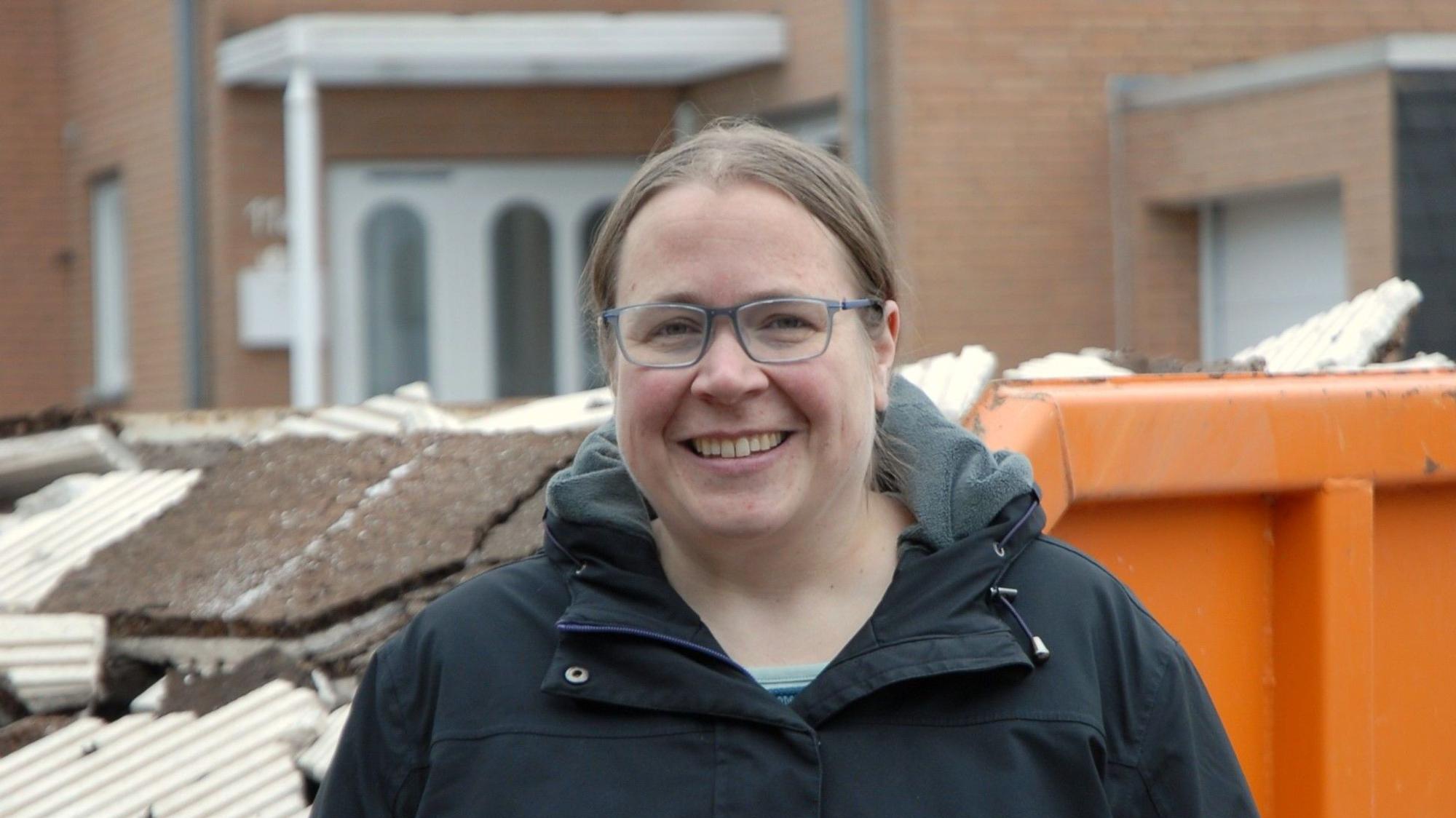 Ein Frau steht vor einem Schuttcontainer und lächelt.
