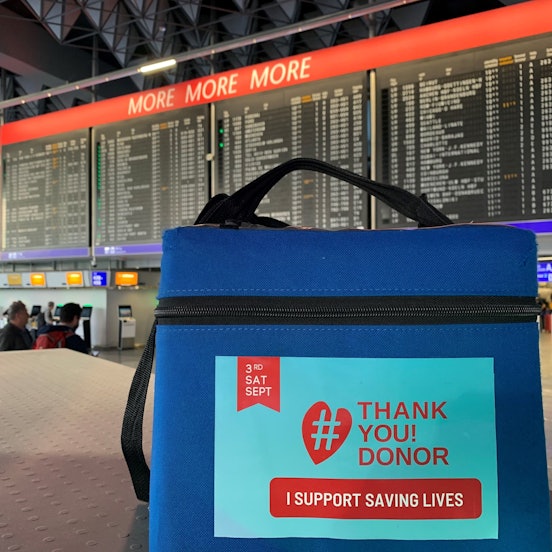Eine blaue Stammzellentransportbox am Frankfurter Flughafen. Im Hintergrund ist die Fluganzeigetafel zu sehen.