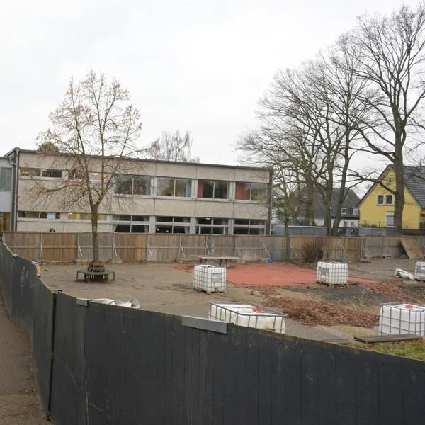 Zwischen dem Schulgebäude und dem Bauzaun sieht man den Gang. Hinter dem Zaun sieht man, den früheren Schulhof.