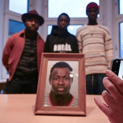 PRODUKTION - 30.01.2024, Nordrhein-Westfalen, Dortmund: Sidy und Lassana Dramé stehen in den Räumen ihrer Rechtsanwältin hinter einem Foto ihres von Polizeischüssen getöteten Bruders Mouhamed Dramé. Im Fall des von Polizeischüssen getöteten Mouhamed Dramé sind Sidy und Lassana Dramé die Nebenkläger in dem Prozess. Sie leben im Senegal und haben für die kommenden drei Monate ein Visum, um den Prozess zu begleiten. Foto: Federico Gambarini/dpa - ACHTUNG: Nur zur redaktionellen Verwendung im Zusammenhang mit der aktuellen Berichterstattung über den Prozess. +++ dpa-Bildfunk +++