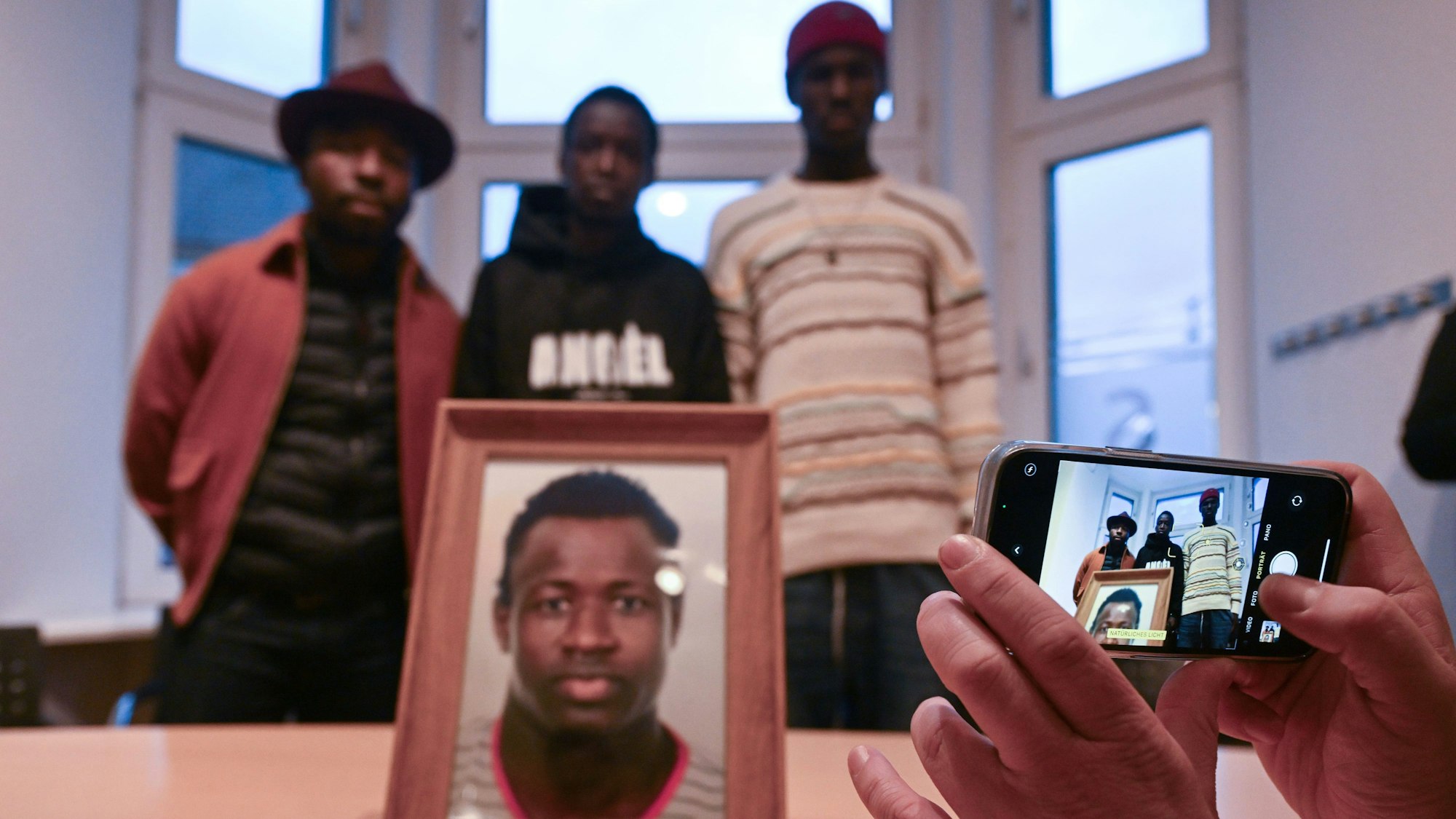 PRODUKTION - 30.01.2024, Nordrhein-Westfalen, Dortmund: Sidy und Lassana Dramé stehen in den Räumen ihrer Rechtsanwältin hinter einem Foto ihres von Polizeischüssen getöteten Bruders Mouhamed Dramé. Im Fall des von Polizeischüssen getöteten Mouhamed Dramé sind Sidy und Lassana Dramé die Nebenkläger in dem Prozess. Sie leben im Senegal und haben für die kommenden drei Monate ein Visum, um den Prozess zu begleiten. Foto: Federico Gambarini/dpa - ACHTUNG: Nur zur redaktionellen Verwendung im Zusammenhang mit der aktuellen Berichterstattung über den Prozess. +++ dpa-Bildfunk +++