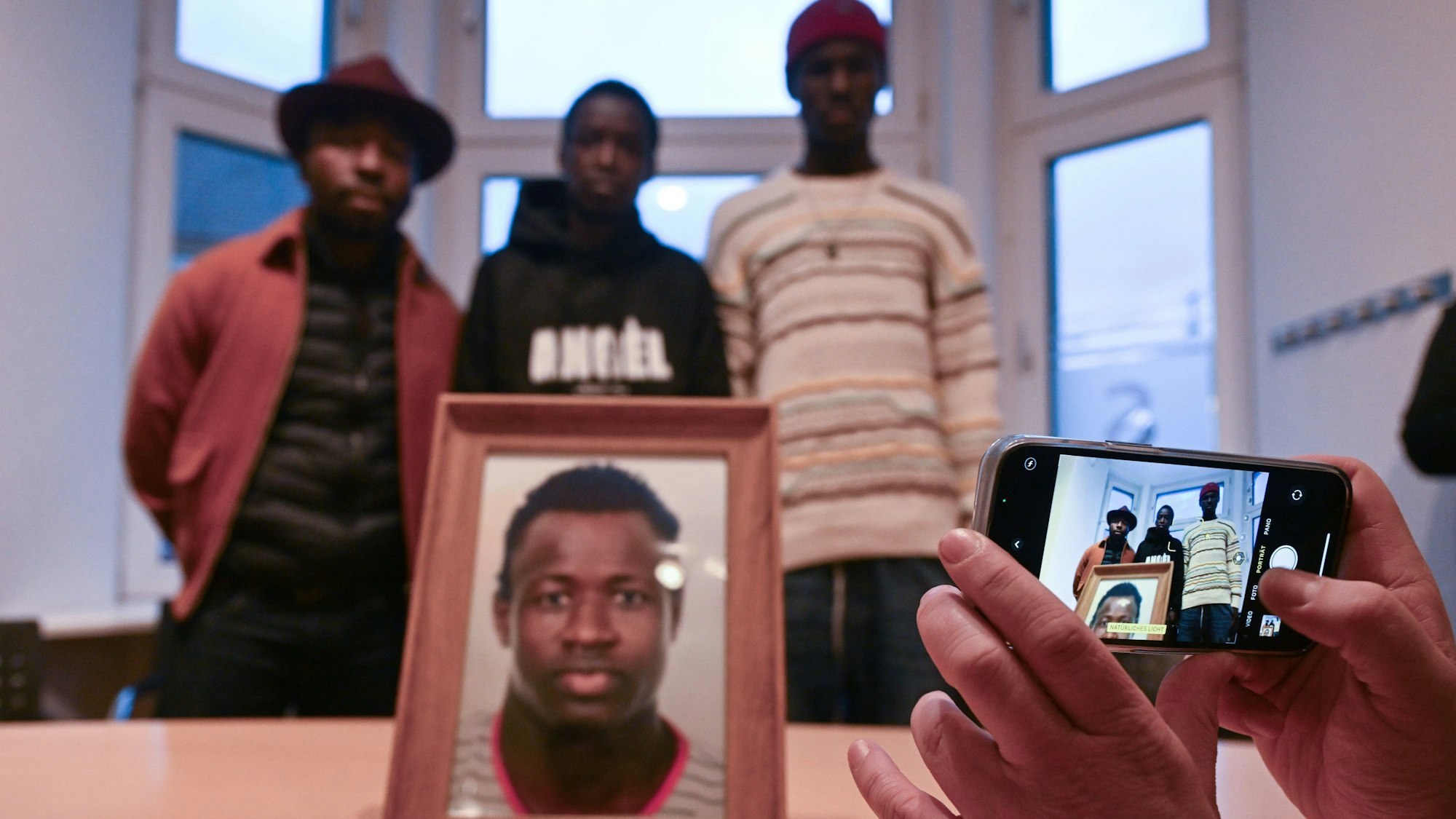 Sidy und Lassana Dramé stehen in den Räumen ihrer Rechtsanwältin hinter einem Foto ihres von Polizeischüssen getöteten Bruders Mouhamed Dramé.