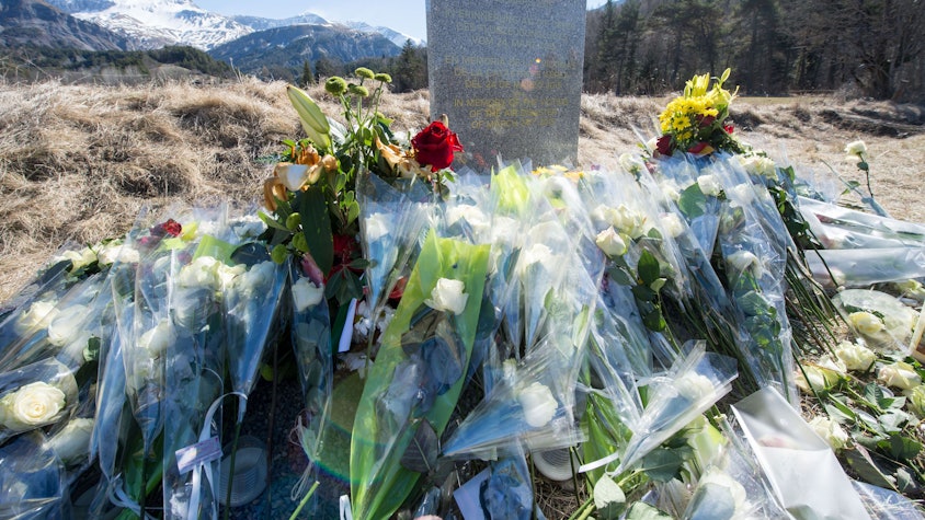 Inmitten von Blumen steht eine steinerne Gedenkstele mit der Aufschrift "In Erinnerung an die Opfer des Flugzeugunglücks vom 24. März 2015" in den vier Sprachen Englisch, Deutsch, Spanisch und Französisch in La Vernet, Frankreich, nahe der Unglücksstelle des abgestürzten Germanwings-Fluges 4U9525 vor dem Bergpanorama.