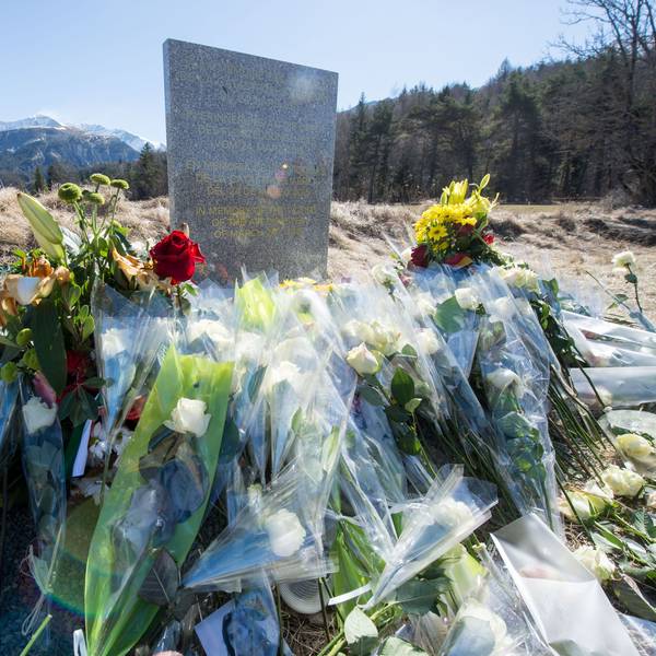 Inmitten von Blumen steht eine steinerne Gedenkstele mit der Aufschrift "In Erinnerung an die Opfer des Flugzeugunglücks vom 24. März 2015" in den vier Sprachen Englisch, Deutsch, Spanisch und Französisch in La Vernet, Frankreich, nahe der Unglücksstelle des abgestürzten Germanwings-Fluges 4U9525 vor dem Bergpanorama.