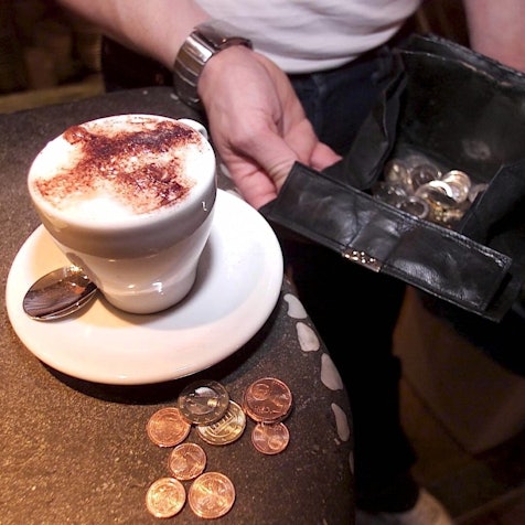 Ein Kellner hält seine Geldbörse auf, um einen bestellten Cappuccino abzukassieren.