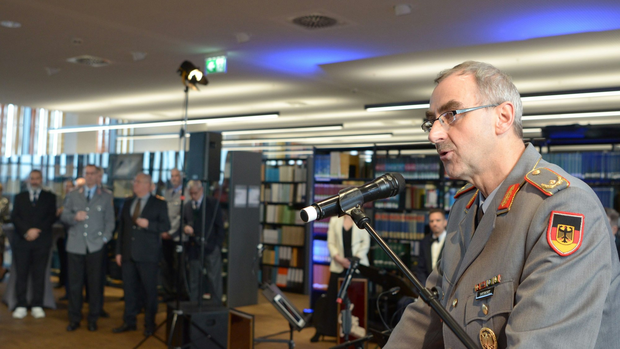 Brigadegeneral Peter Webert spricht ins Mikrofon, im Hintergrund Zuhörer und die Bibliothek der Fachinformationsstelle, die gerade ihren Neubau bezogen hat.