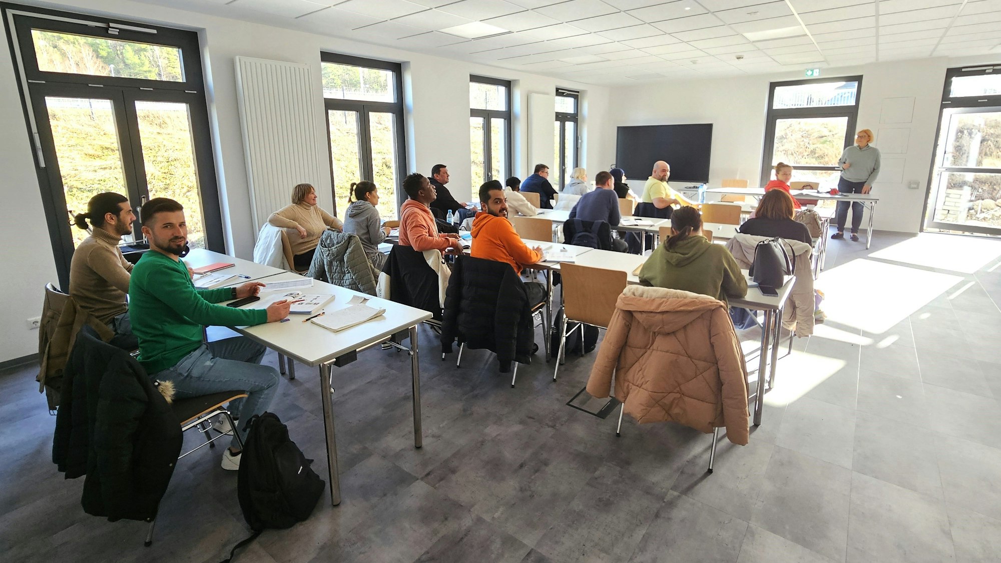 Teilnehmer eines Integrationskurses sitzen wie in einer Schulklasse an Tischen.