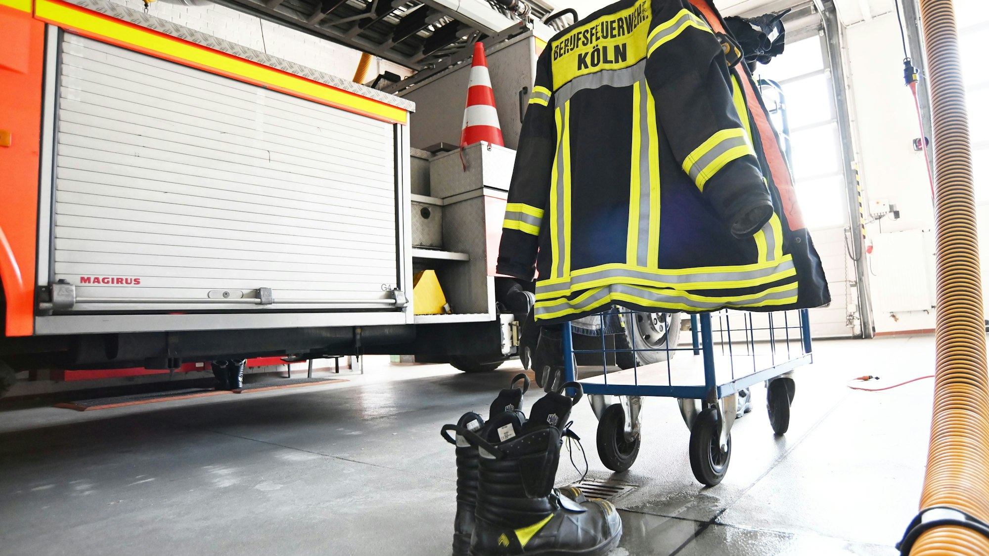 Eine Feuerwehruniform hängt über einem Haken, im Hintergrund steht eine Feuerwehrauto.