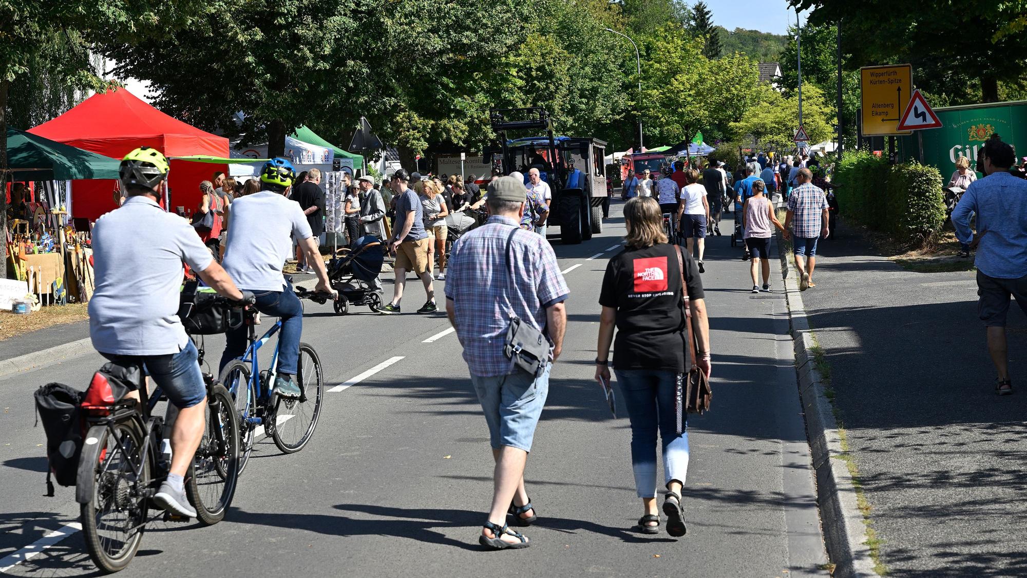 Zu sehen ist eine Straße, auf der Fußgänger schlendern und Fahrradfahrer unterwegs sind.