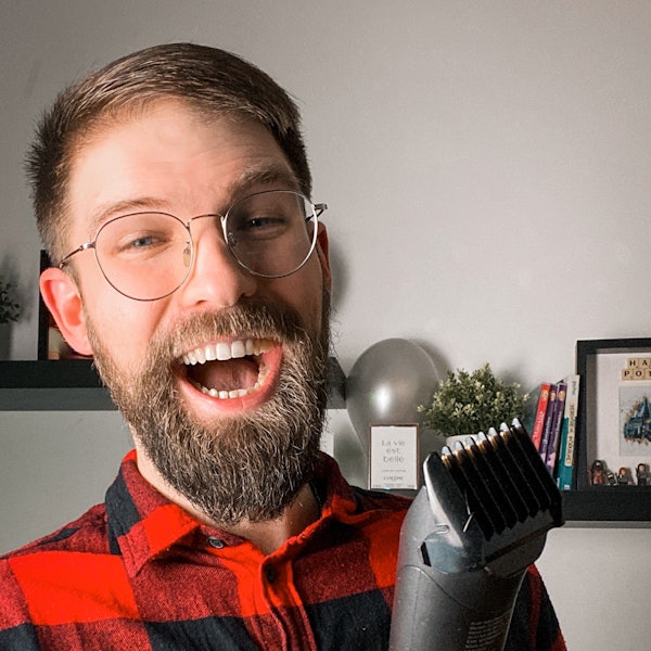 Lachender junger Mann mit Bart, Brille und Rasierer in der Hand