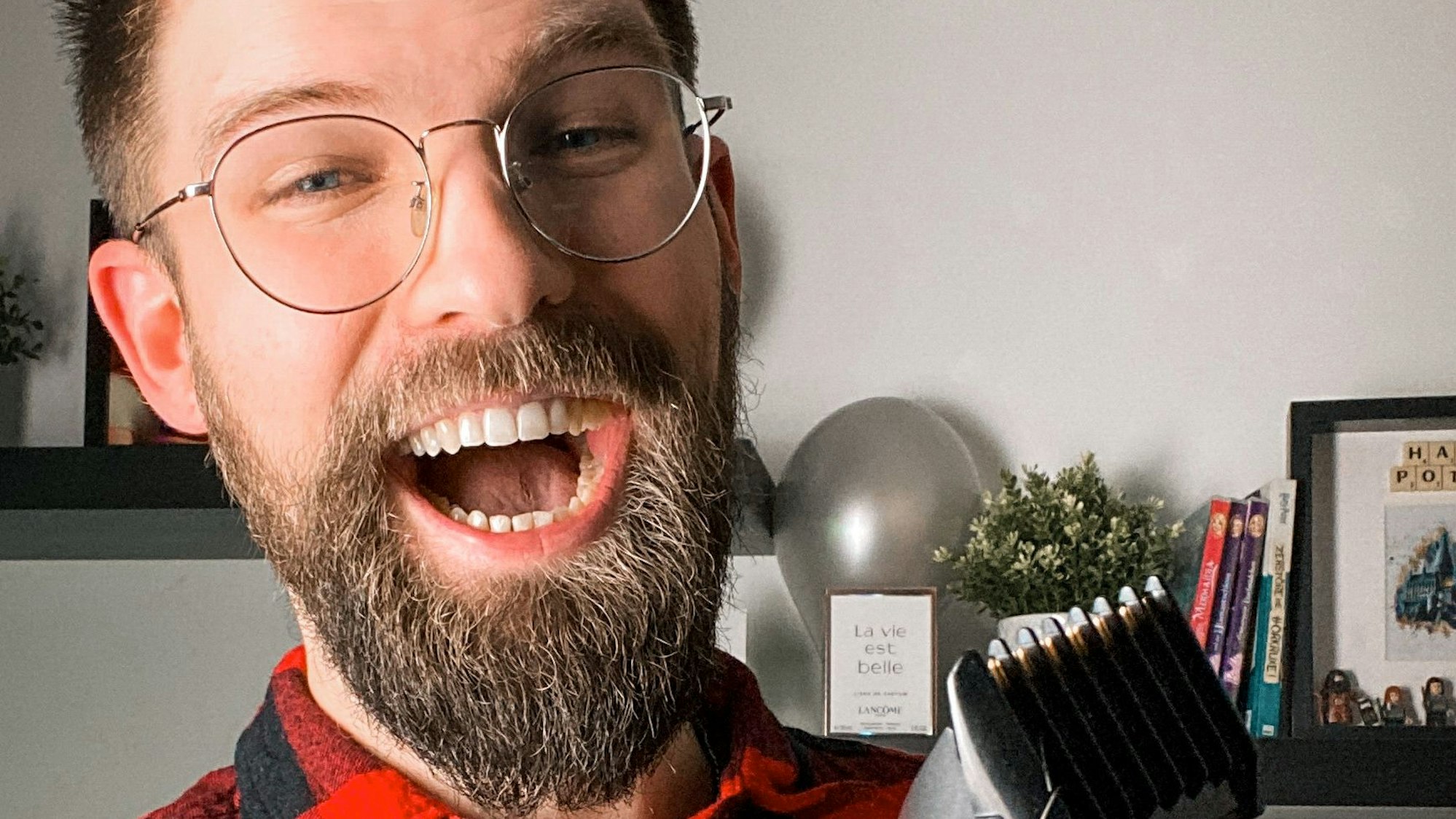 Lachender junger Mann mit Bart, Brille und Rasierer in der Hand