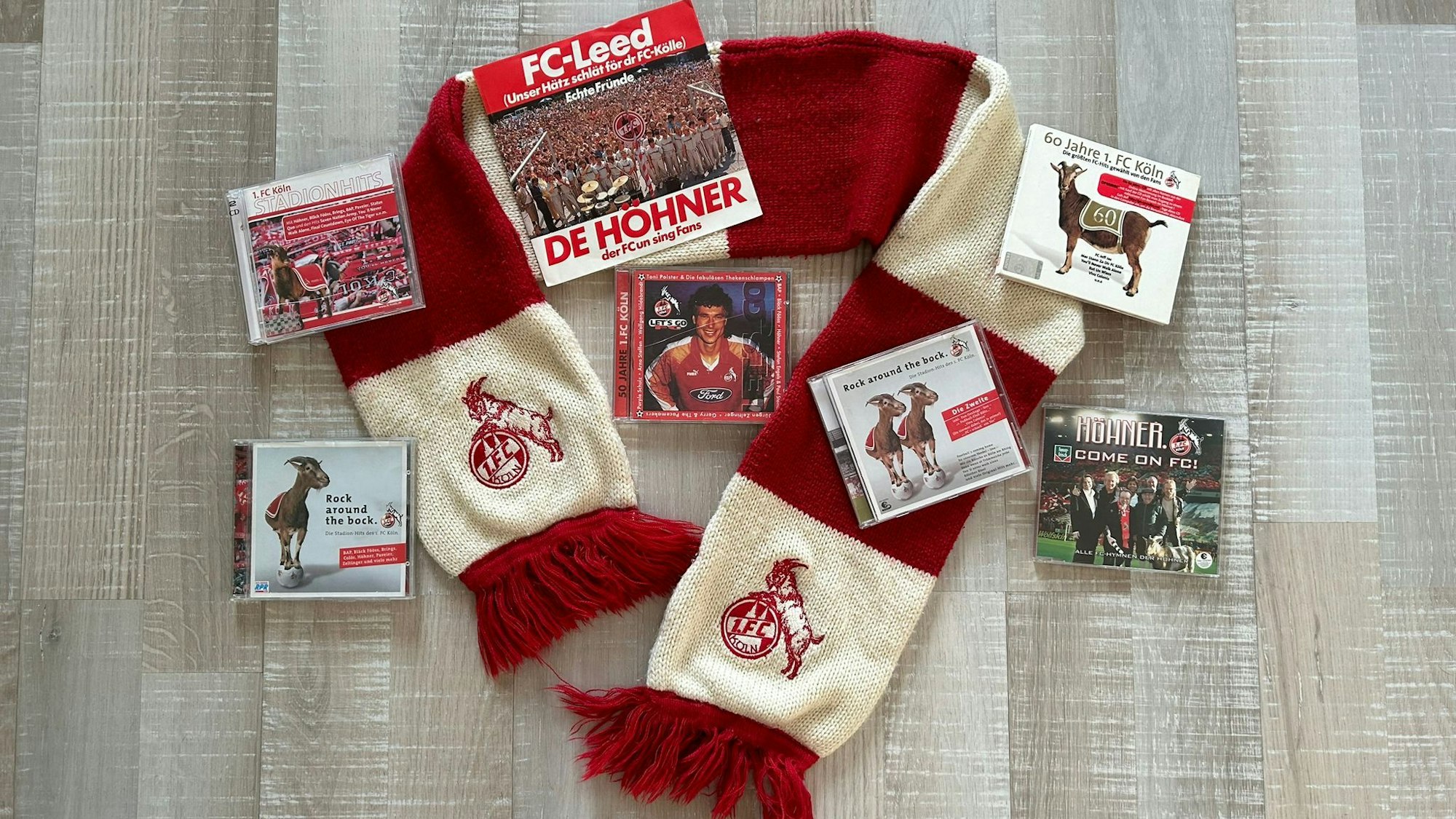 Auf einem rot-weißen Fan-Schal des 1. FC Köln sind verschiedene CDs sowie eine Schallplatte mit Liedern über den Verein drapiert.