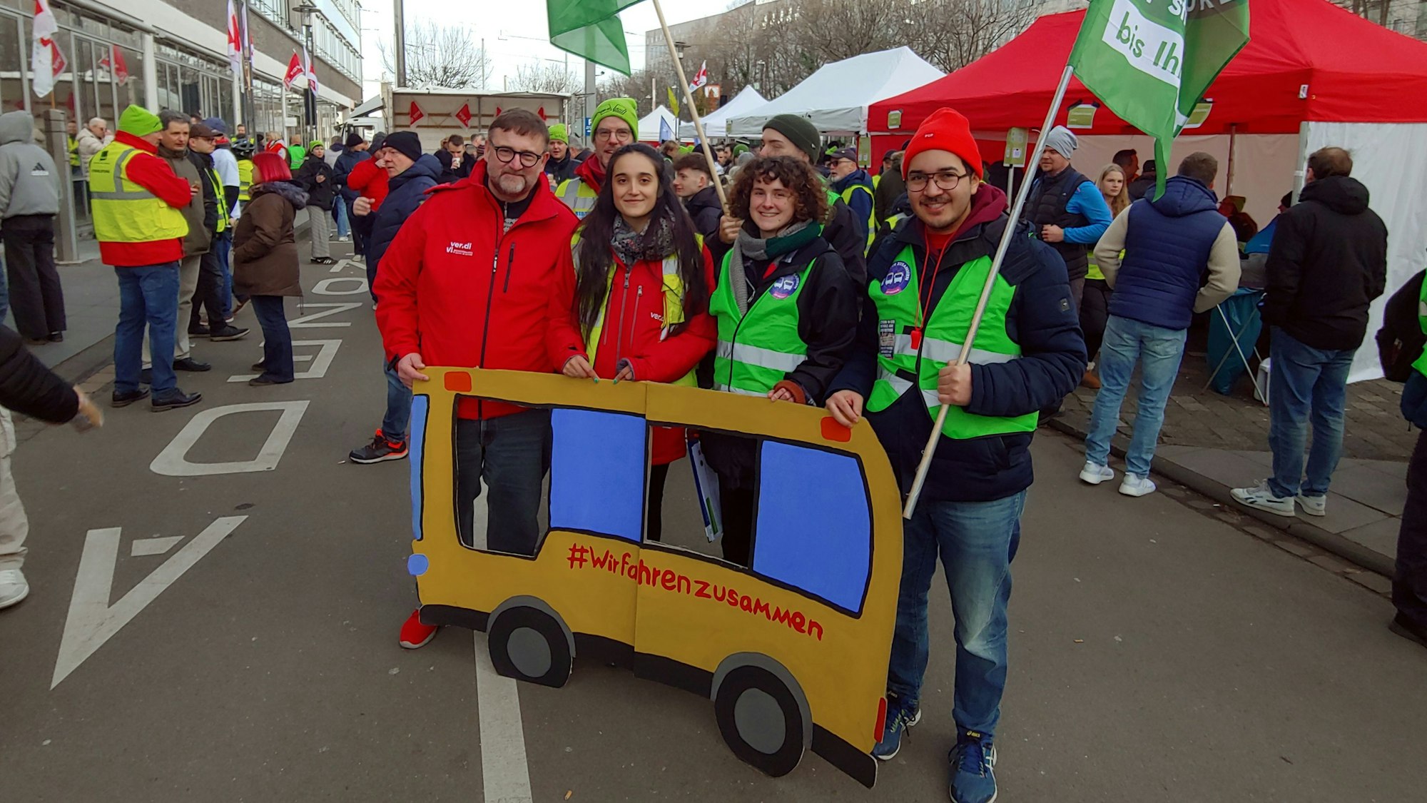 Zu sehen sind Streikende der KVB und der Umweltgruppe „Fridays for Future“ mit einem Plakat aus Pappe, das einen Bus darstellt. Er trägt die Aufschrift „#Wir fahrenzusammen“.