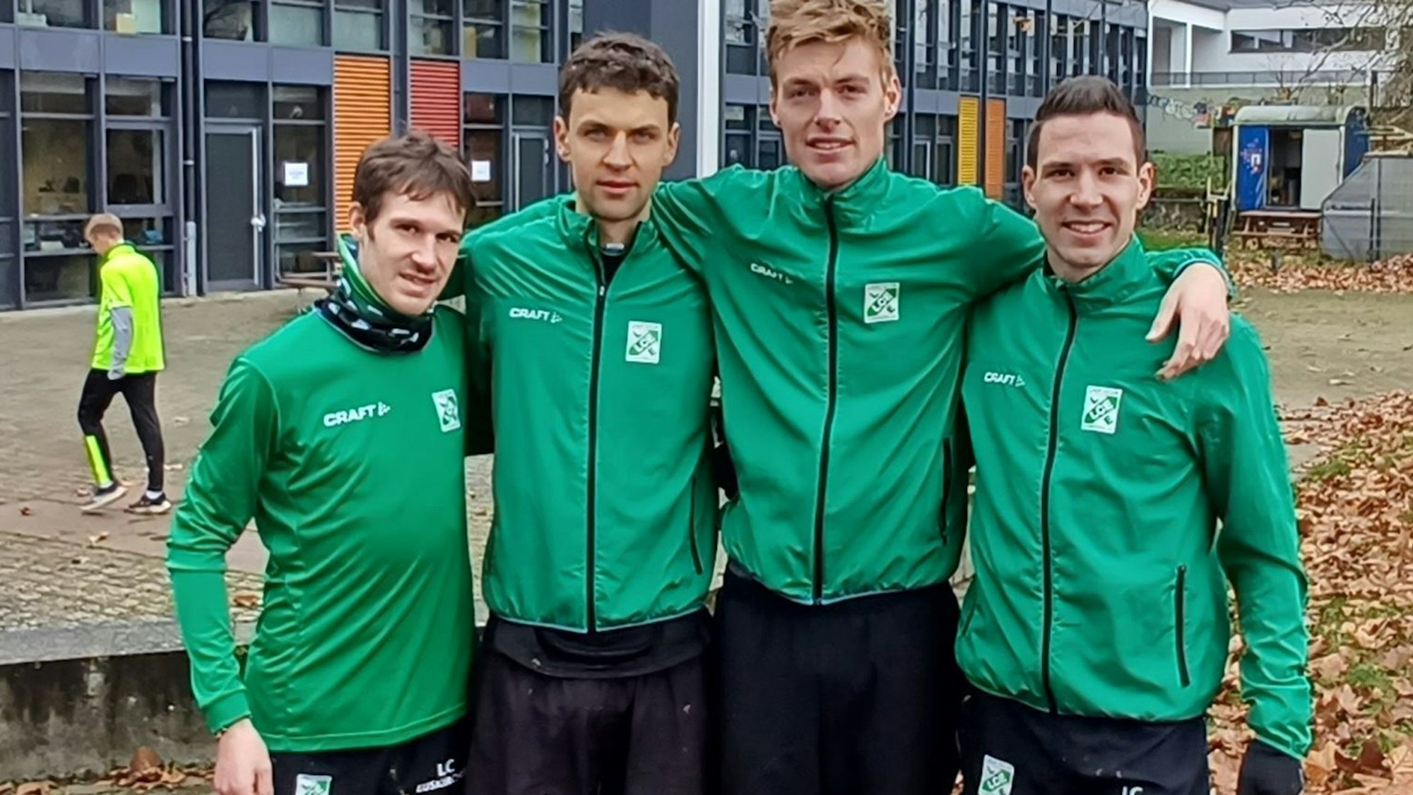 In grüner und schwarzer Trainingskleidung stehen vier Crossläufer des LC Euskirchen Arm in Arm nebeneinander.