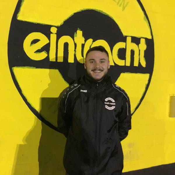 Ömer Tokac im Porträt vor einer gelben Wand mit schwarzem Eintracht-Schriftzug.