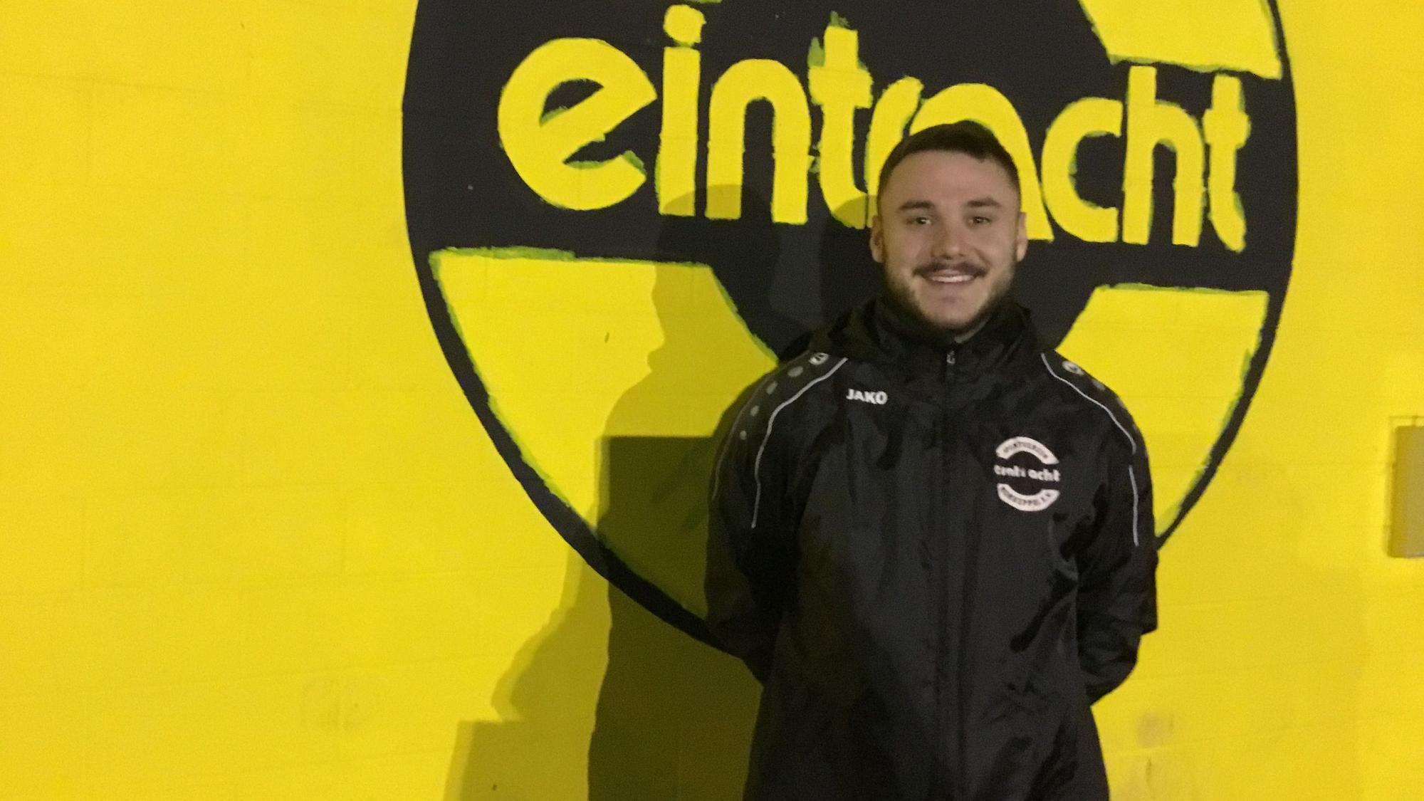 Ömer Tokac im Porträt vor einer gelben Wand mit schwarzem Eintracht-Schriftzug.