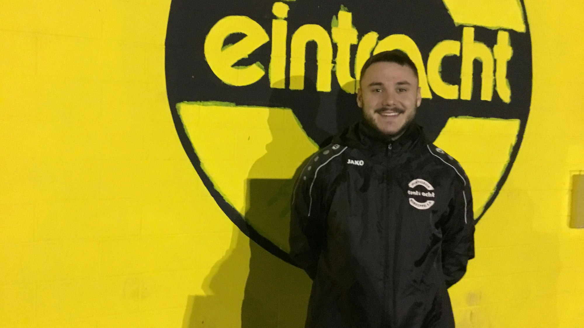 Ömer Tokac im Porträt vor einer gelben Wand mit schwarzem Eintracht-Schriftzug.