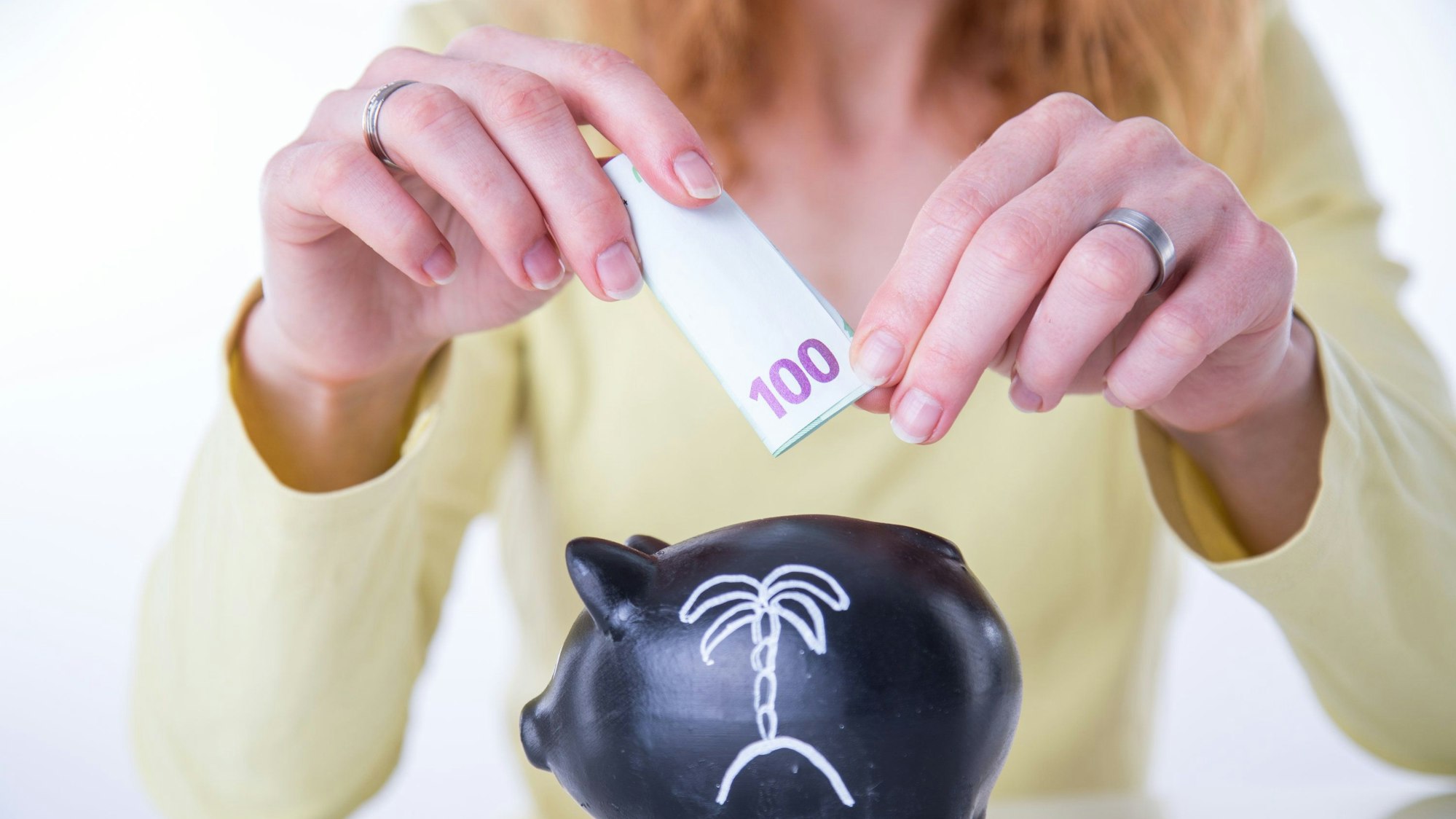 Eine Frau steckt einen 100-Euro-Schein in ein Sparschwein.