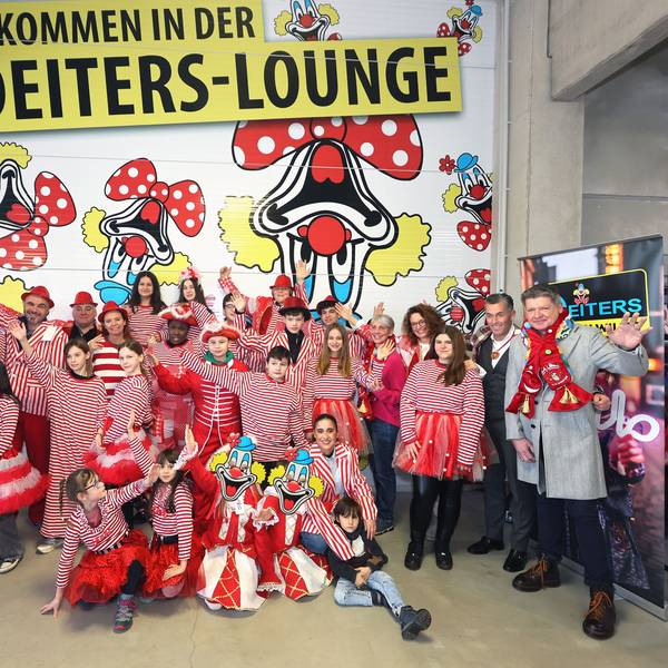 Bewohner und Betreuer der Brücker „KidS“-Wohnheime sind mit Kostümen in rot-weiß verkleidet und stehgen vor einer Wand der Deiters-Filiale in Frechen.