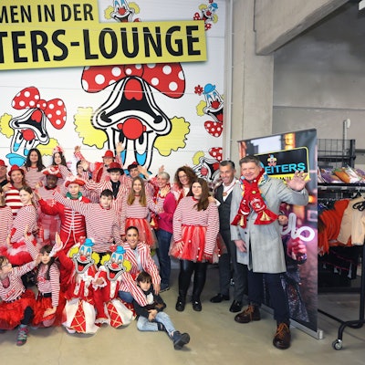 Bewohner und Betreuer der Brücker „KidS“-Wohnheime sind mit Kostümen in rot-weiß verkleidet und stehgen vor einer Wand der Deiters-Filiale in Frechen.