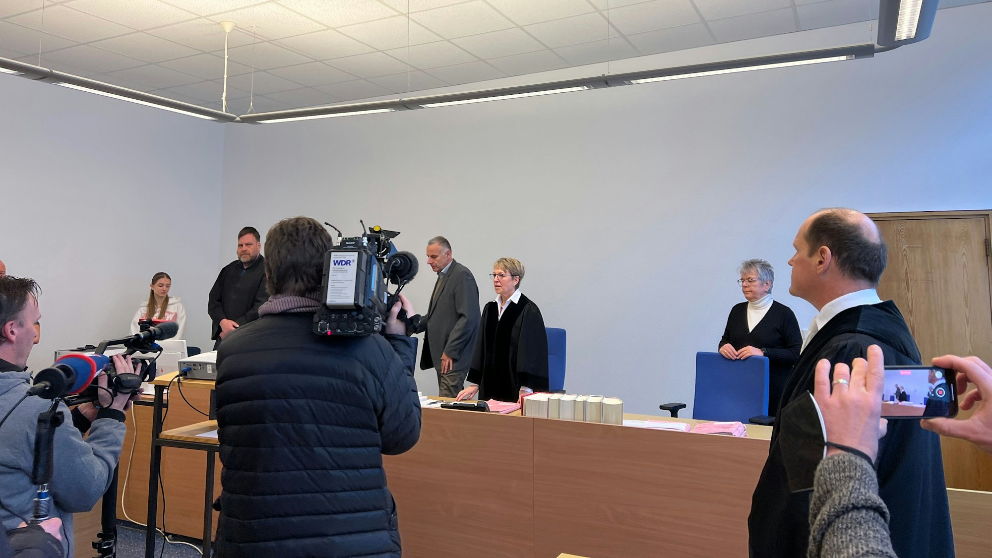 Journalisten filmen und fotografieren das Bensberger Schöffengericht vor Beginn des ersten Prozesses gegen einen der Kölner Nizza-Hooligans. In der Mitte Schöffenrichterin Birgit Brandes, eingerahmt von Schöffe und Schöffin, rechts Oberstaatsanwalt Ulf Willuhn, der die Anklage vertrat.