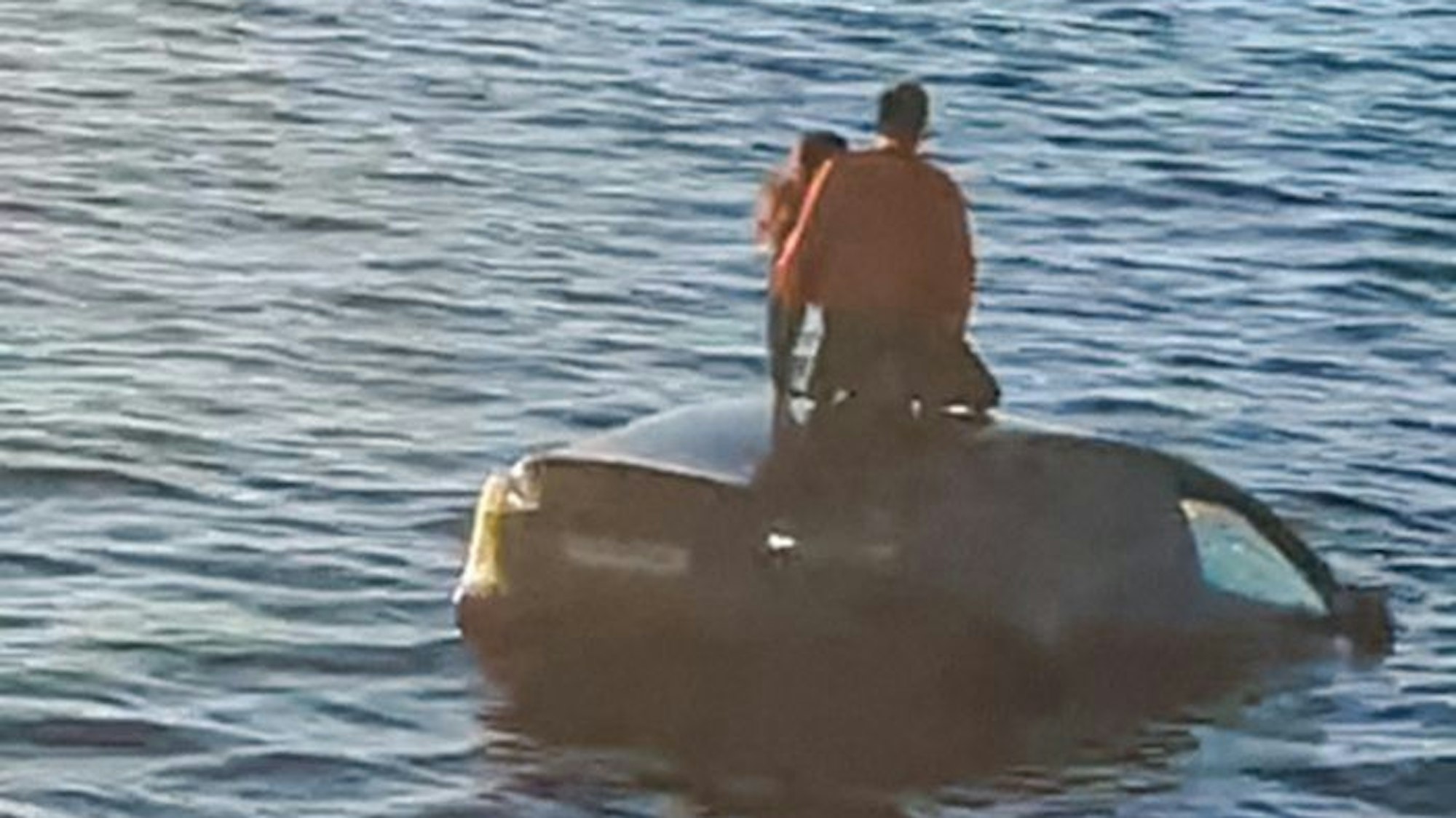 Zwei Personen stehen auf einem Auto, das im Begriff ist, in einem Fjord zu versinken.