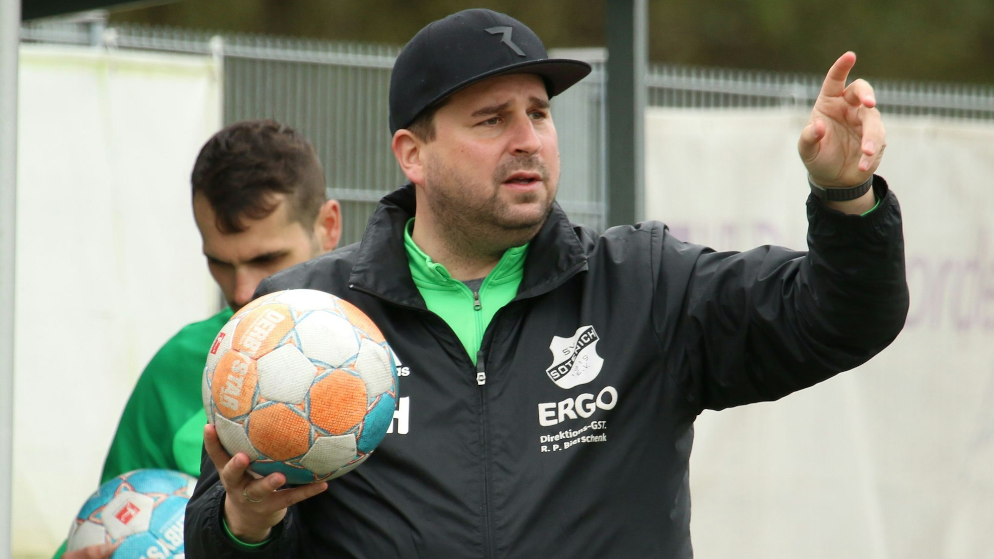 Das Bild zeigt Christian Hammes, der einen Ball in der rechten Hand hält. Mit der linken zeigt er in Richtung Sportplatz.