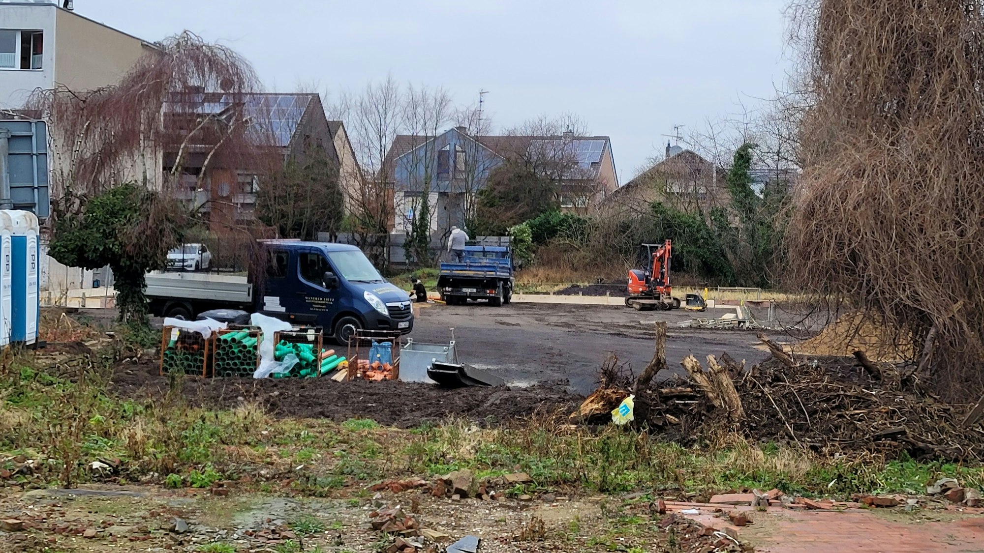 Im Hintergrund eines großen Baufeldes sind ein paar Arbeiter, ein Bagger und mehrere Fahrzeuge zu sehen.
