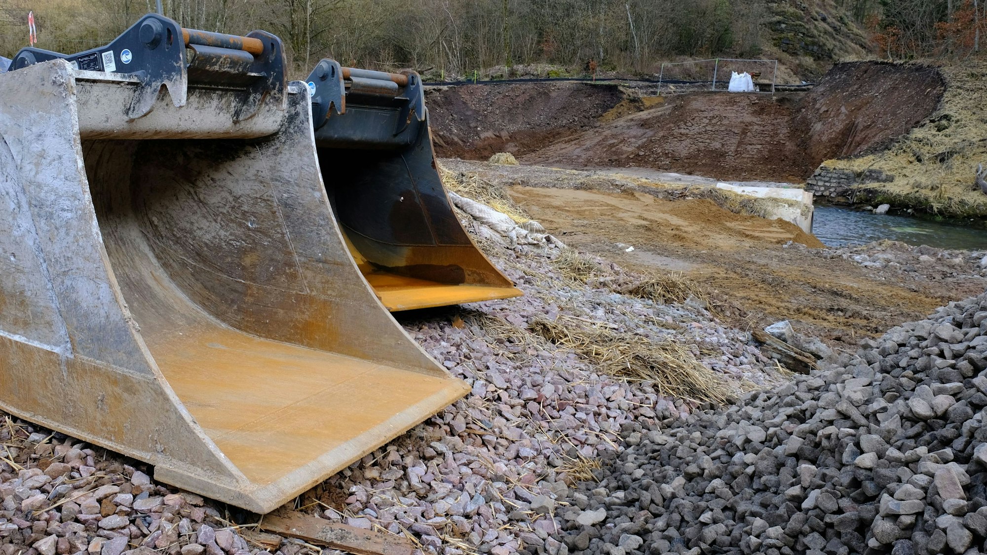 Zwei große Baggerschaufeln sind an einer Baustelle der im Wiederaufbau befindlichen Eifelstrecke abgestellt worden. Die Bauarbeiten ruhen.