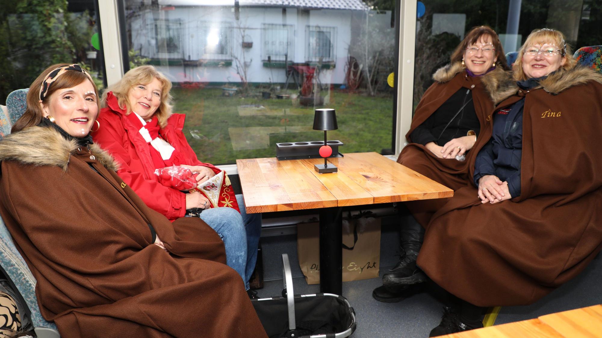 Vier kostümierte Frauen sitzen an einem Tisch in einem Linienbus.