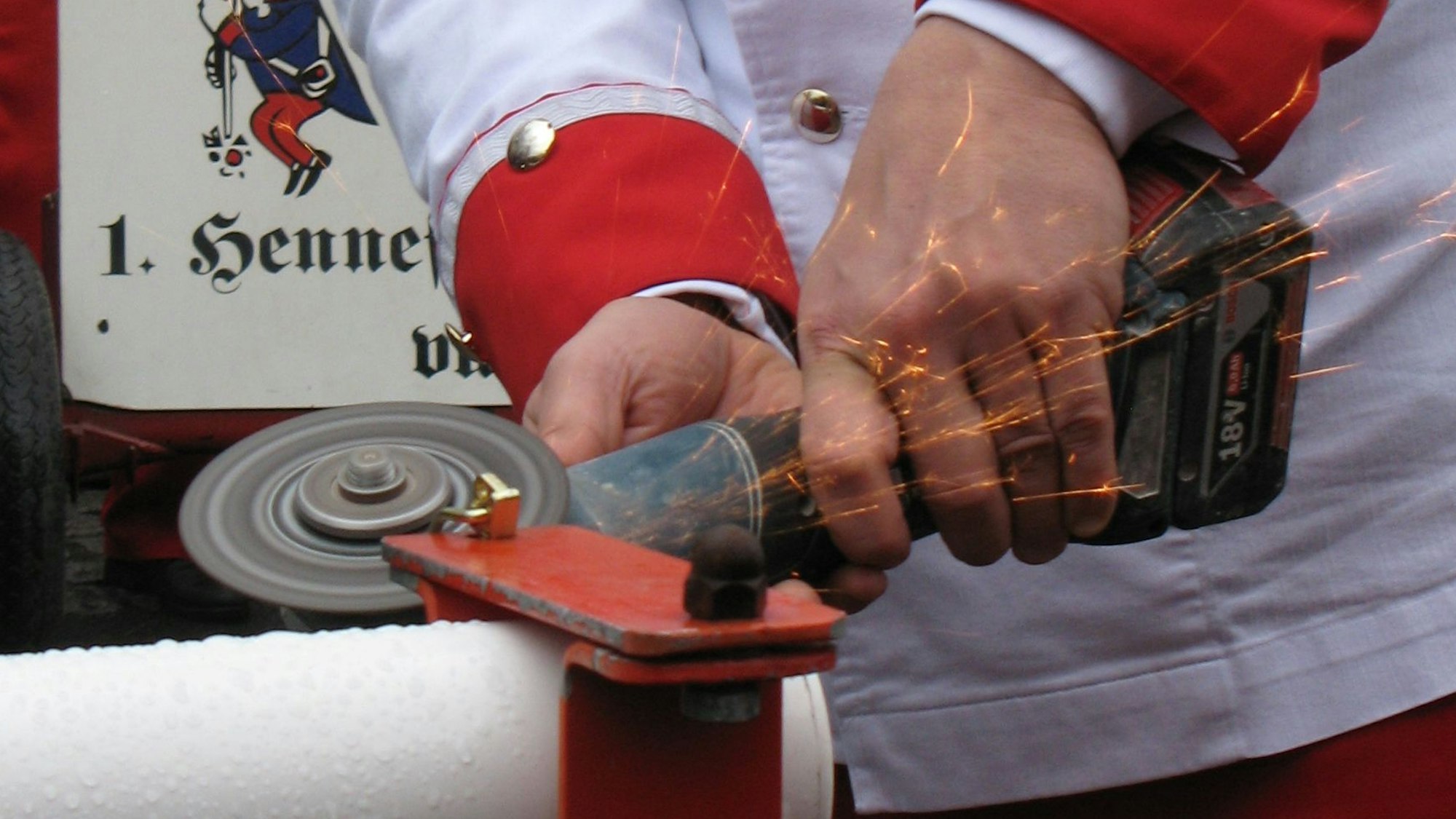 Hände mit einem Winkelschleifer, der an einer Schranken-Arretierung angelegt wird, Funken sprühen.