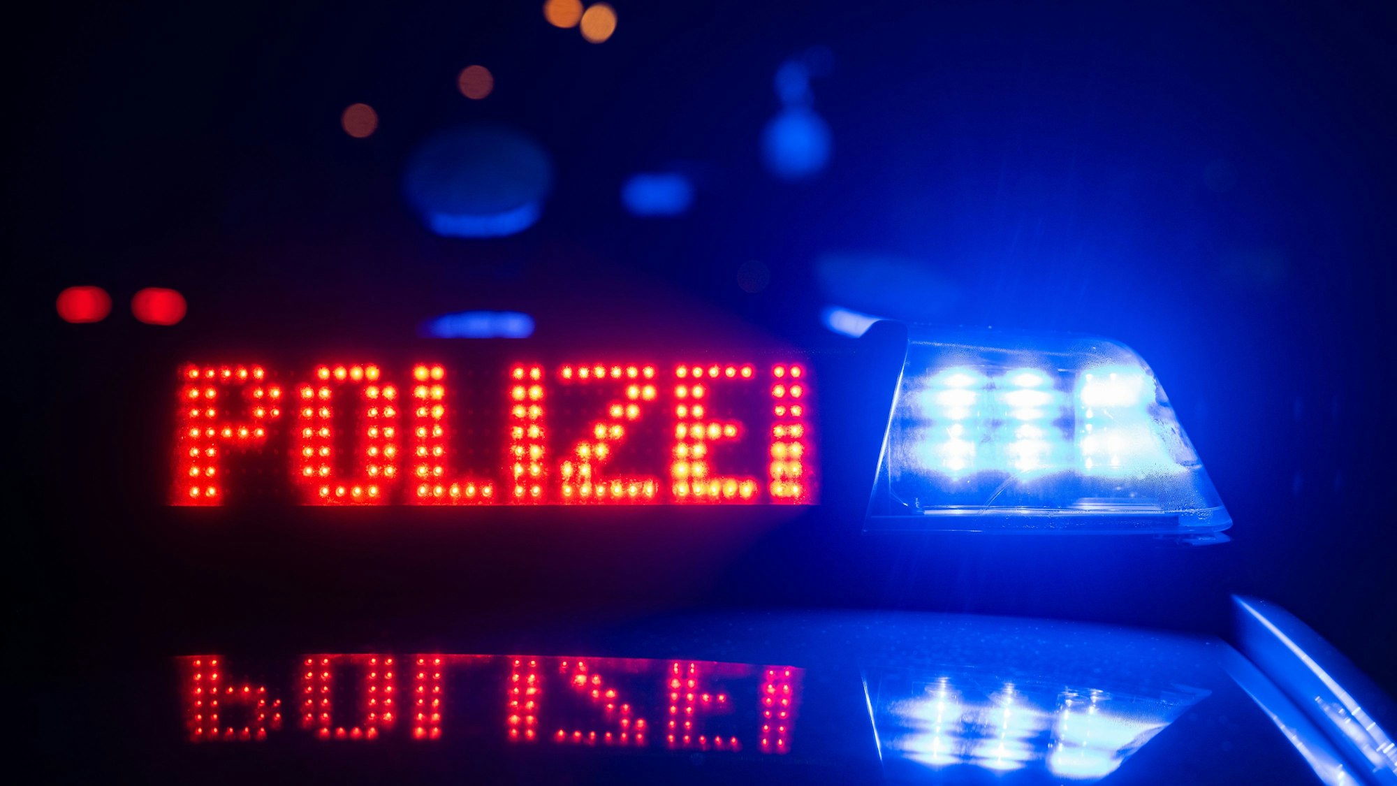 Eine Polizeischrift leuchtet neben einem Blaulicht an einem Abend auf einem Polizeiwagen.