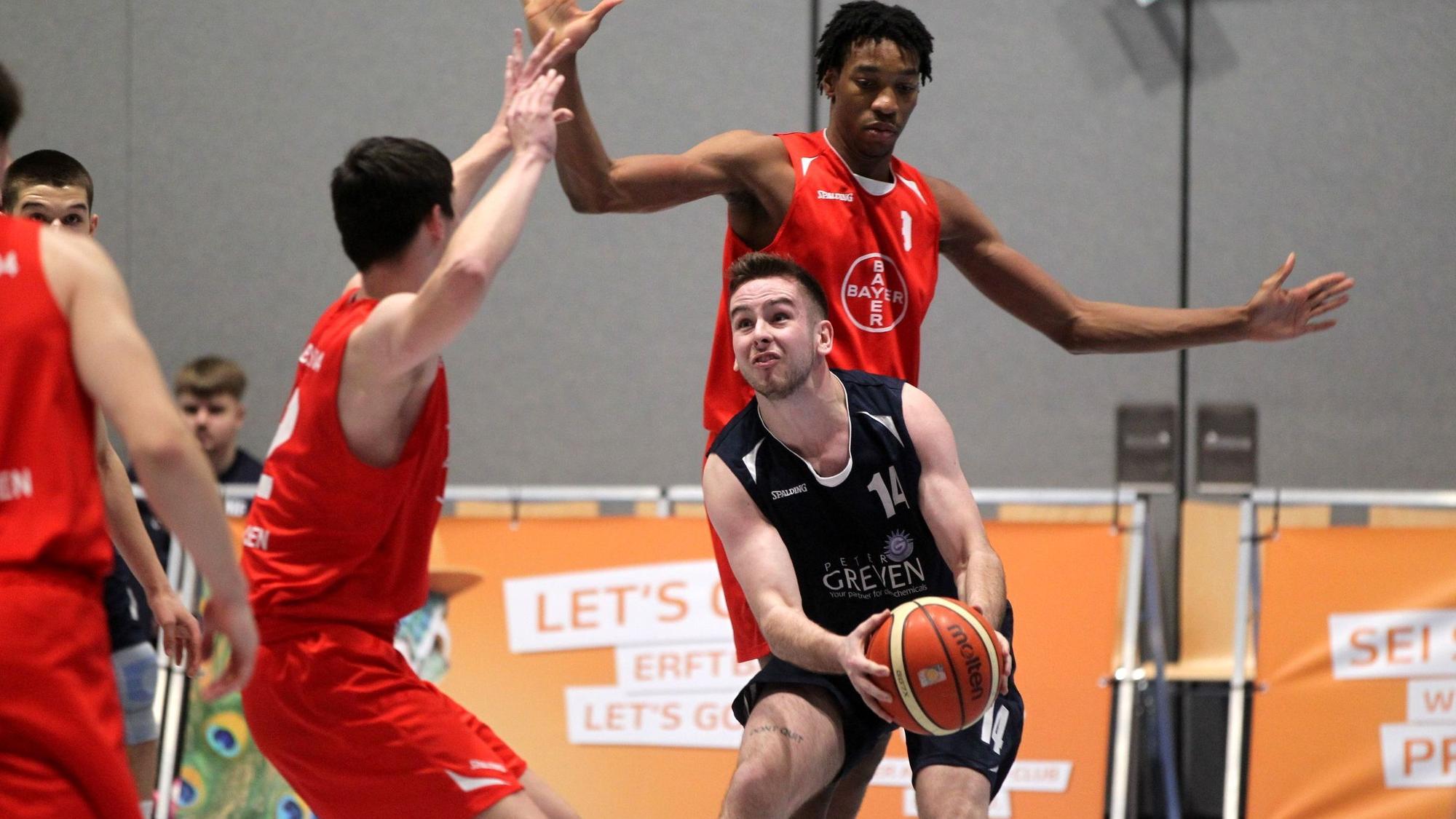 Erftbaskets-Spieler Chris Beier geht mit dem Ball in den Händen leicht in die Knie. Dadurch wirken seine Gegenspieler umso größer.
