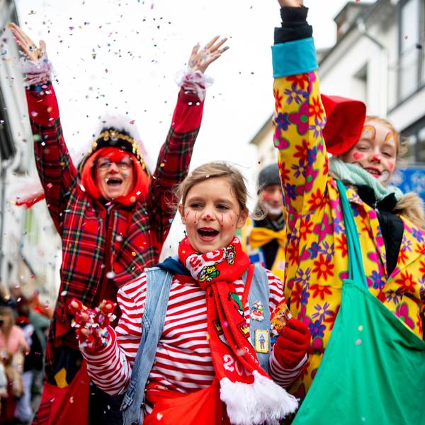 Das Bild zeigt drei Jecke während des Kinderzugs. Die haben gerade Konfetti in die Luft geworfen.