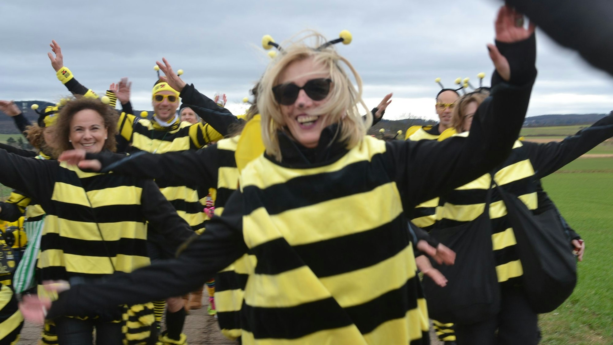 Frauen und Männer haben sich als Hummeln kostümiert und tanzen durch das Bild.