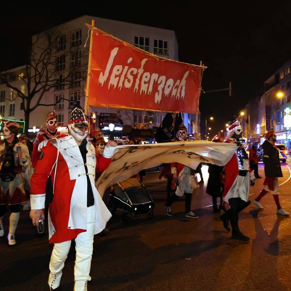 Verkleidete gehen mit einem Plakat auf dem Jeisterzoch steht über eine Straße