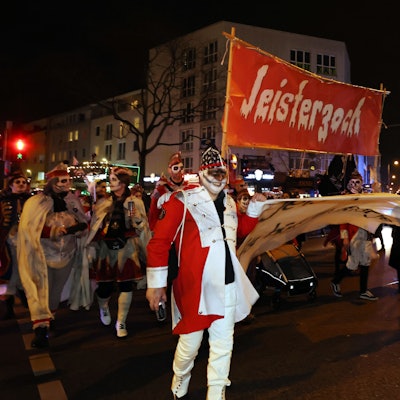 Verkleidete gehen mit einem Plakat auf dem Jeisterzoch steht über eine Straße