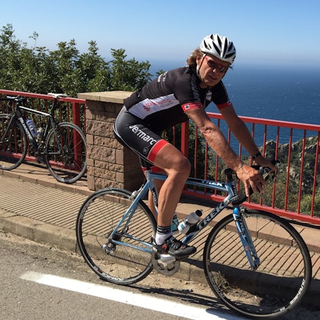 Ein Mann fährt Rennrad, hinter ihm ist das blaue Meer zu sehen.