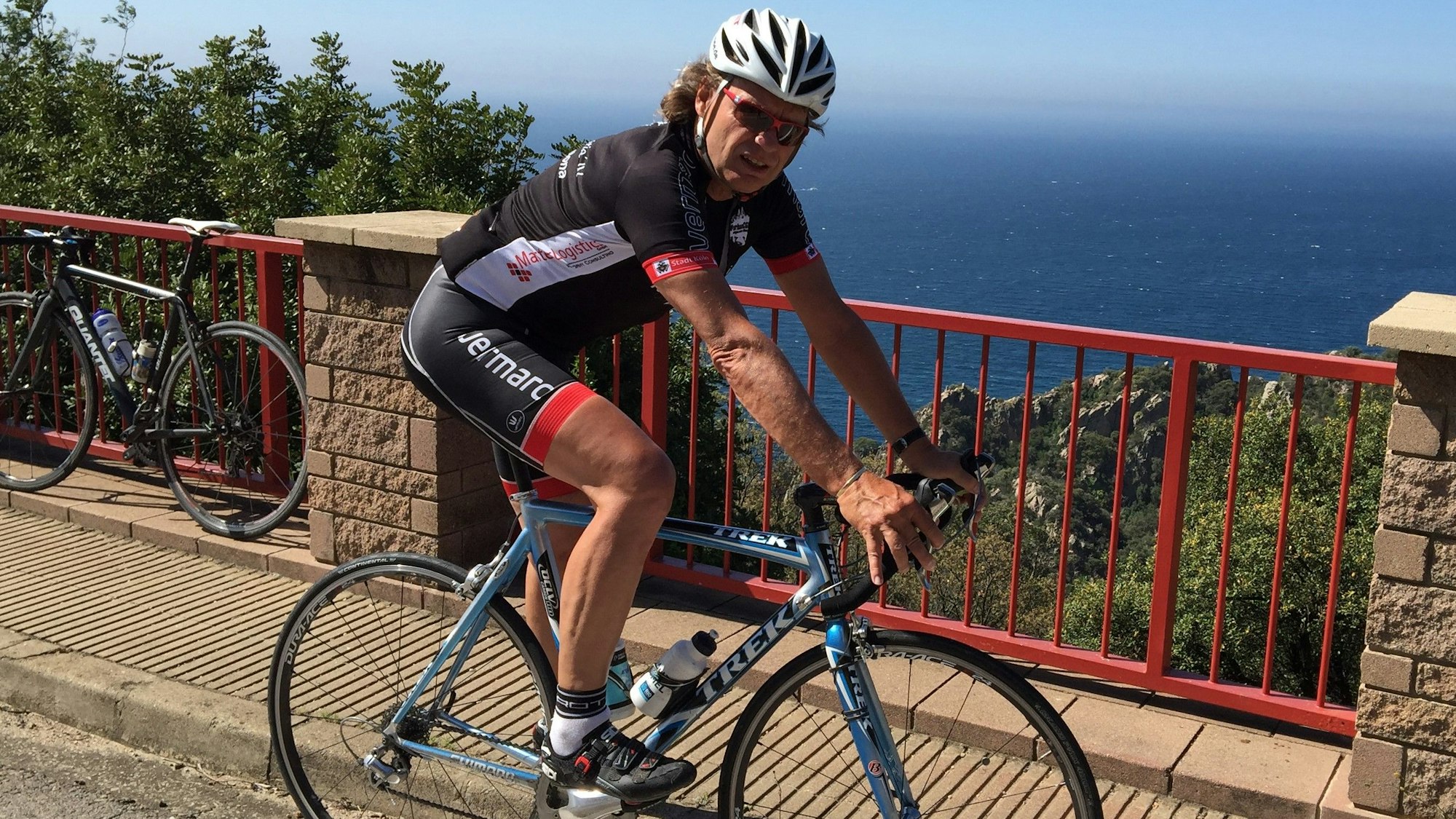 Ein Mann fährt Rennrad, hinter ihm ist das blaue Meer zu sehen.