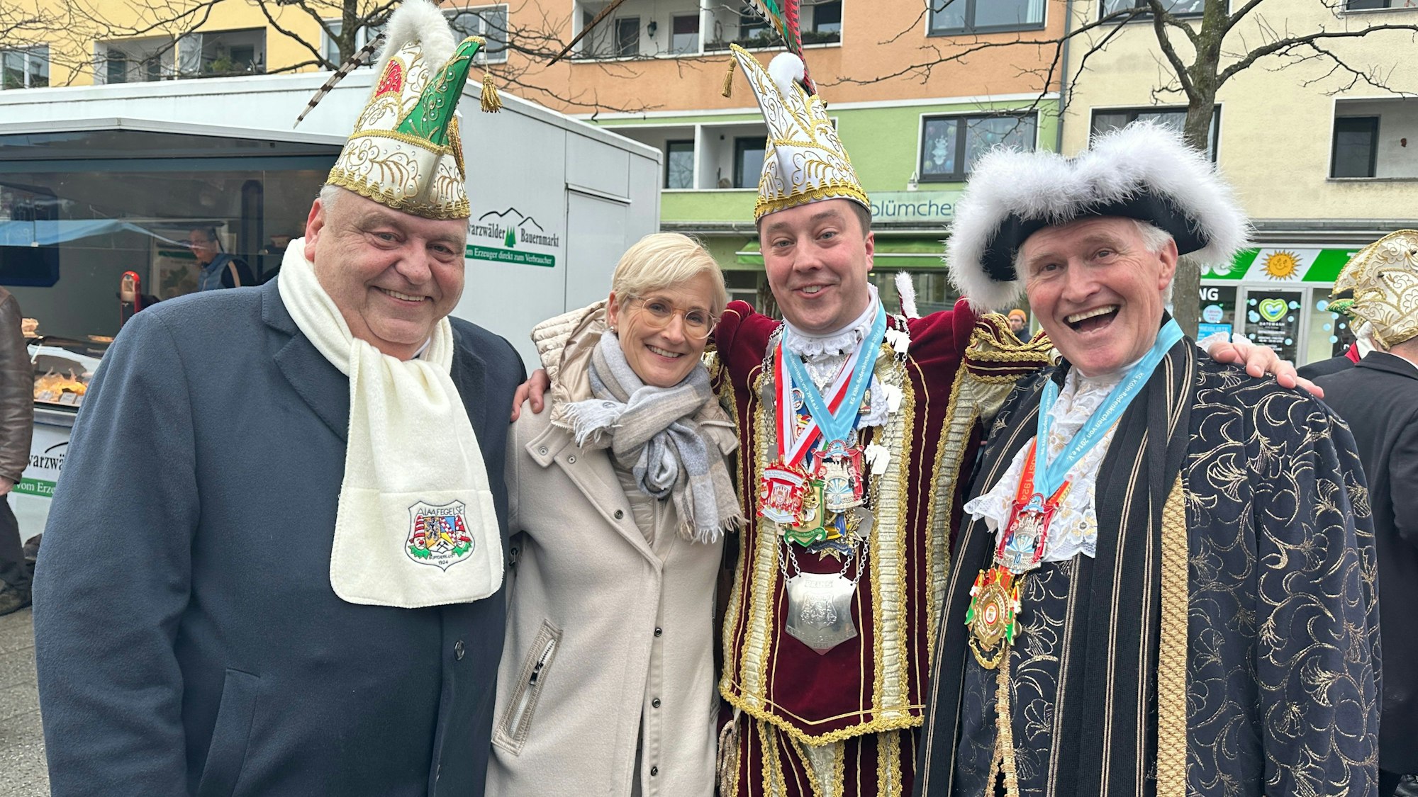 Drei Herren in Kostümen und eine unkostümierte Frau stehen nebeneinander.