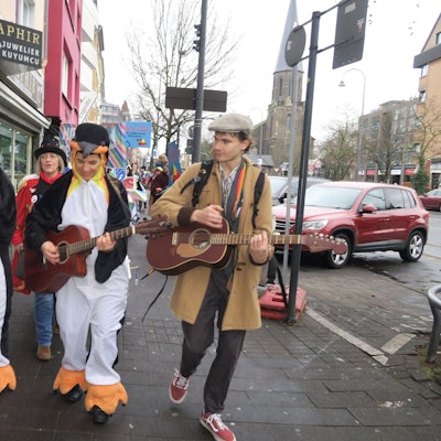 Mit Gitarren und Saxofon zieht eine Gruppe eine Straße entlang.