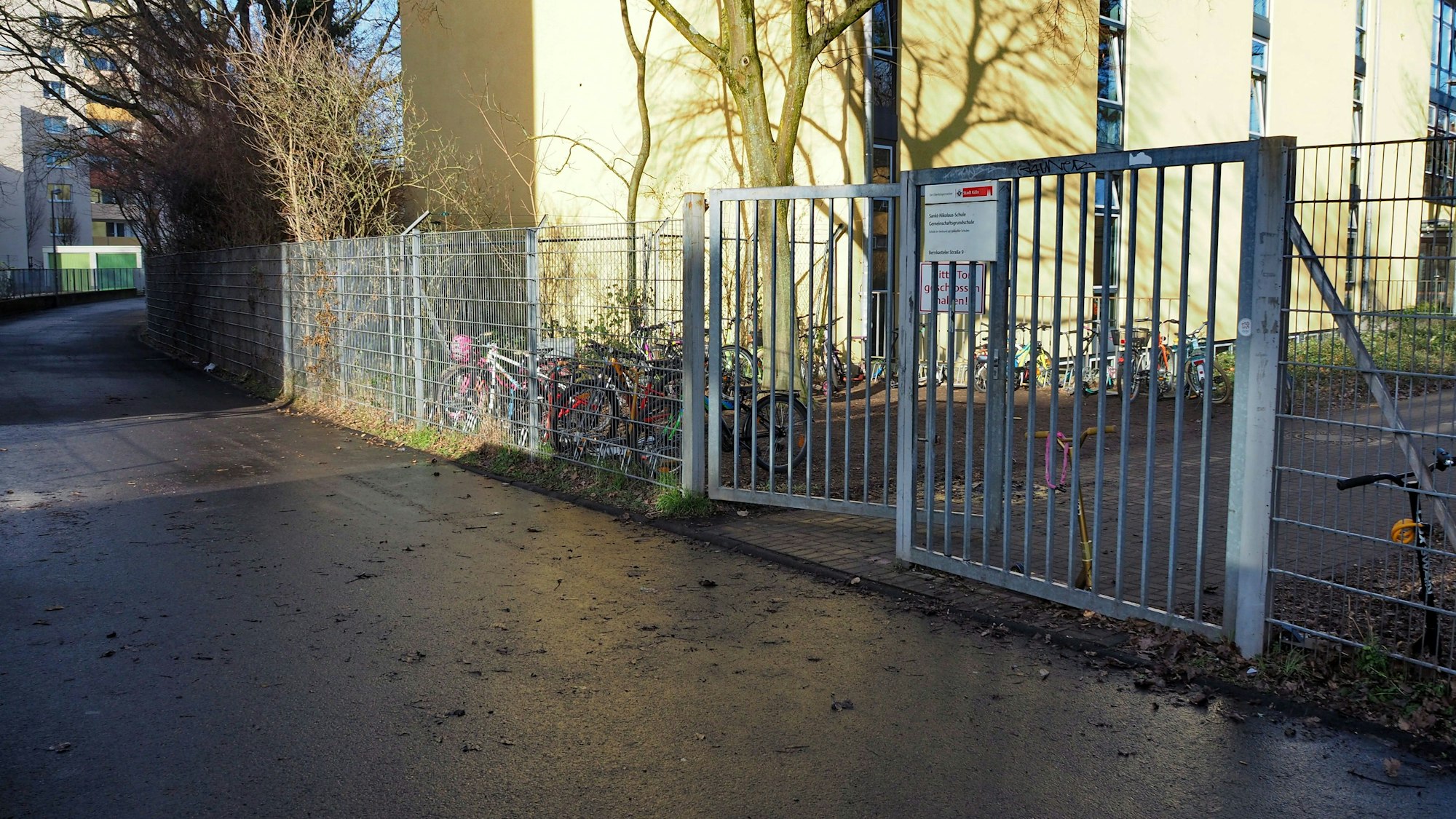An einem Tor zu einem Schulgelände führt ein breiter Weg entlang.