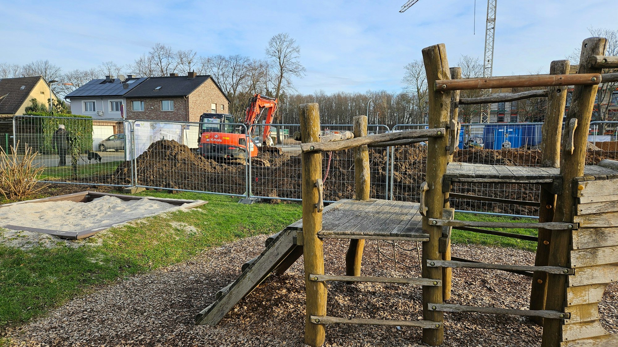 Hinter einem Klettergerüst ist eine Baustelle mit Bagger und Bauzaun.